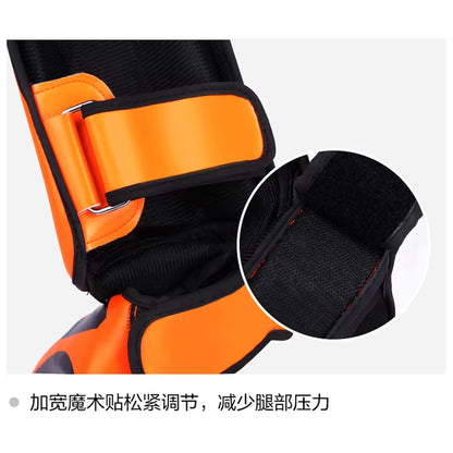 Close-up of kickboxing shin guard pads featuring adjustable strap and soft PU leather material in bright orange.
